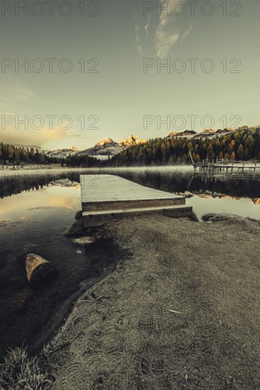 Lake Staz near Sankt Moritz in the Engadin in Switzerland. Morning atmosphere with fog in autumn. Water reflection and snow-covered mountains in the background