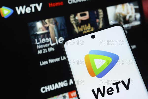 Dhaka, Bangladesh- 28 July 2025: WeTV logo is displayed on a smartphone screen, with the website is visible on a computer screen in the background