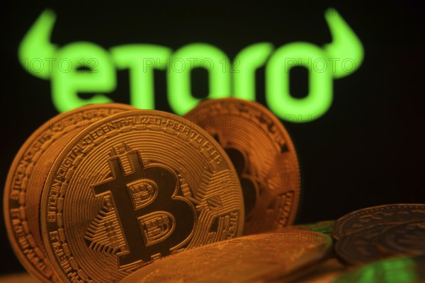 Dhaka, Bangladesh- 27 March 2025: Close-up of Bitcoin coins with the eToro logo visible on a screen in the background