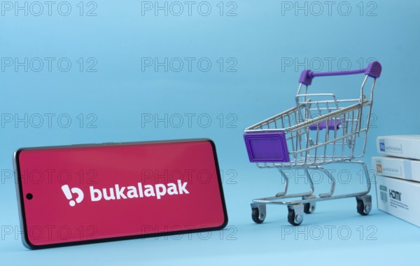 Dhaka, Bangladesh- 03 July 2025: Smartphone with Bukalapak logo next to a small shopping cart and boxes against a blue background