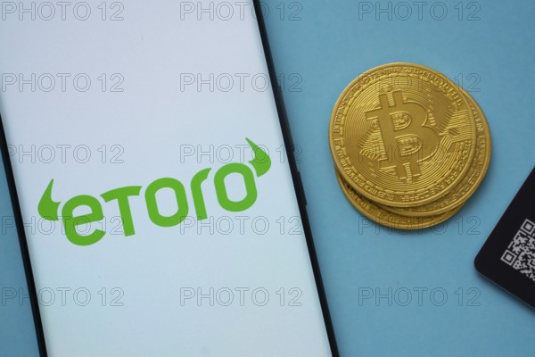 Dhaka, Bangladesh- 22 June 2025: eToro logo on smartphone screen near Bitcoin coin and QR code on blue background