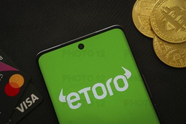Dhaka, Bangladesh- 15 July 2025: Smartphone displaying eToro logo surrounded by Bitcoin coins and payment cards