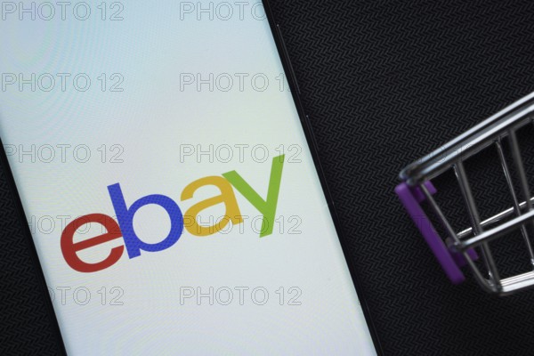 Dhaka, Bangladesh- 03 July 2025: A smartphone displaying the eBay logo next to a miniature shopping cart on a background