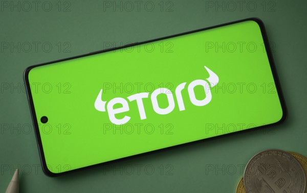 Dhaka, bangladesh- 12 June 2025: eToro logo displayed on a smartphone with Bitcoin coins on a green background
