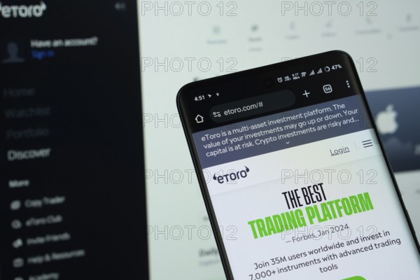 Dhaka, Bangladesh - 15 July 2025: The logo of eToro is displayed on a smartphone screen, and the website the eToro is visible on a computer screen in the background