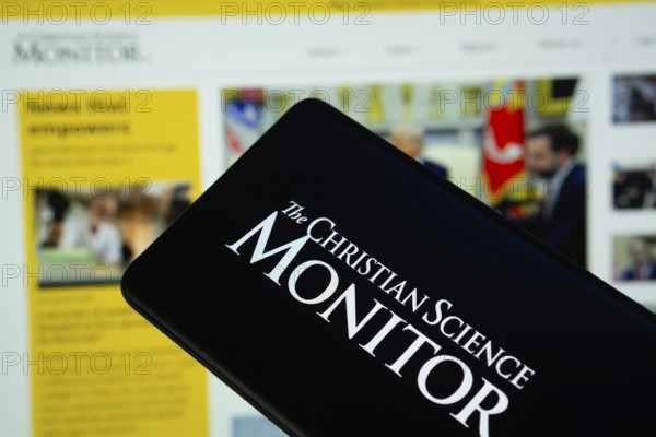 Dhaka, Bangladesh - 18 March 2025: The logo of The Christian Science Monitor is displayed on a smartphone screen, and the website is visible on a computer screen in the background