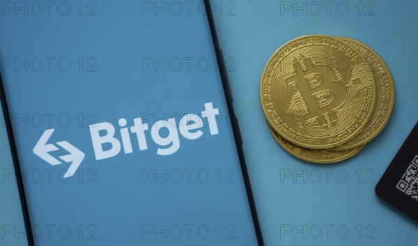 Dhaka, Bangladesh- 22 July 2025: Bitget logo on smartphone screen near Bitcoin coin and QR code on blue background