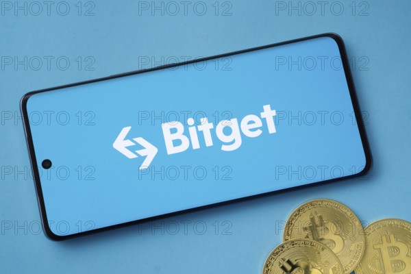 Dhaka, Bangladesh- 27 July 2025: Bitget logo displayed on a smartphone with Bitcoin coins on a blue background