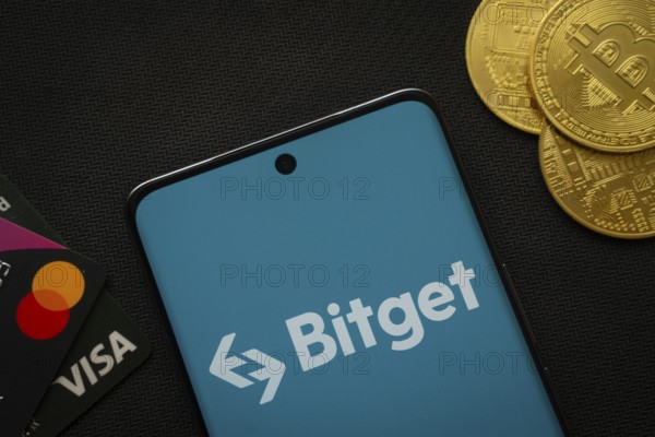 Dhaka, Bangladesh- 27 July 2025: Smartphone displaying Bitget logo surrounded by Bitcoin coins and payment cards