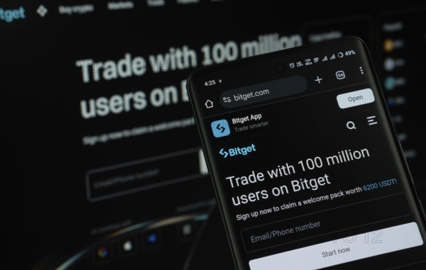 Dhaka, Bangladesh - 27 July 2025: The logo of Bitget is displayed on a smartphone screen, and the website the bitget is visible on a computer screen in the background