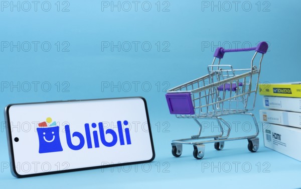 Dhaka, Bangladesh- 03 July 2025: Smartphone with Blibli logo next to a small shopping cart and boxes against a blue background