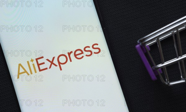 Dhaka, Bangladesh- 03 July 2025: A smartphone displaying the AliExpress logo next to a miniature shopping cart on a background