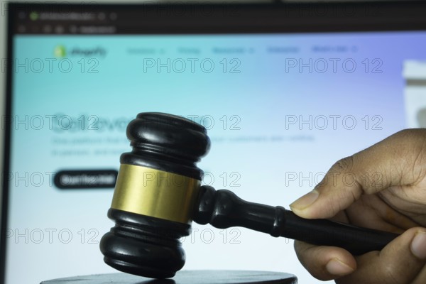 Dhaka, Bangladesh- 20 June 2025: A hand holds a gavel in front of a computer screen displaying Shopify's website