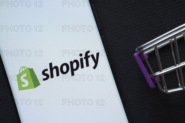 Dhaka, Bangladesh- 03 July 2025: A smartphone displaying the Shopify logo next to a miniature shopping cart on a background
