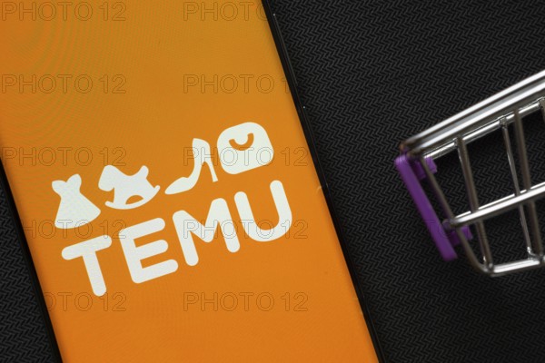 Dhaka, Bangladesh- 03 July 2025: A smartphone displaying the Temu logo next to a miniature shopping cart on a background