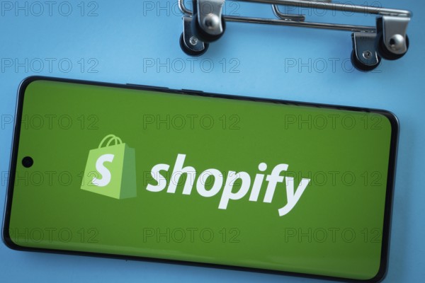 Dhaka, Bangladesh- 03 July 2025: Smartphone screen showing the Shopify logo with shopping cart wheels on a blue background