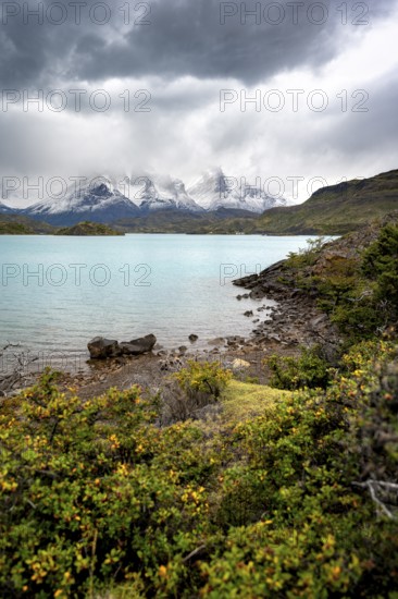 Cloudy mountain range Cuernos del Paine, shore of the blue lake Lago Pehoe in the evening light, dramatic sky, Torres del Paine National Park, Chile