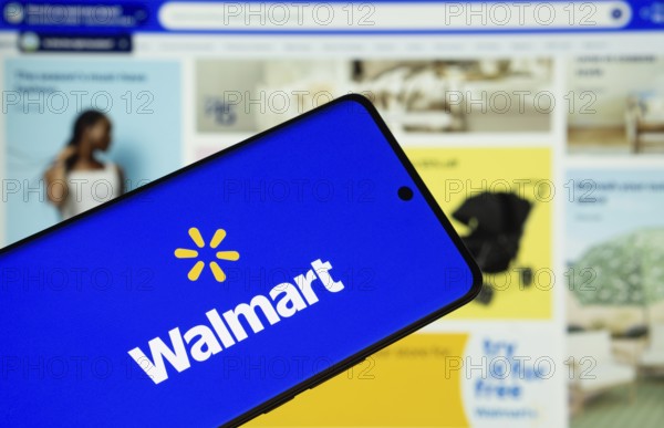 Dhaka, Bangladesh- 15 July 2025: Walmart logo is displayed on a smartphone screen, with the website visible on a computer screen in the background