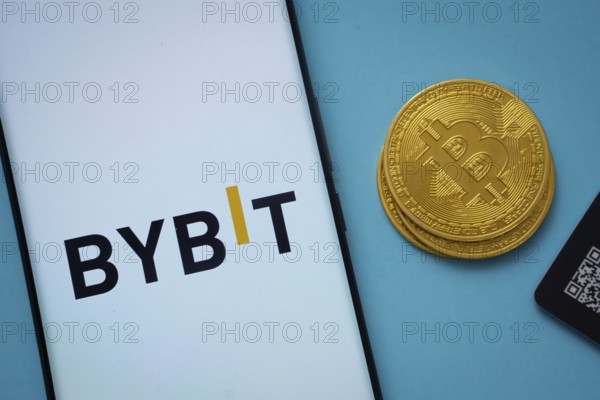 Dhaka, Bangladesh- 15 July 2025: Bybit logo on smartphone screen near Bitcoin coin and QR code on blue background