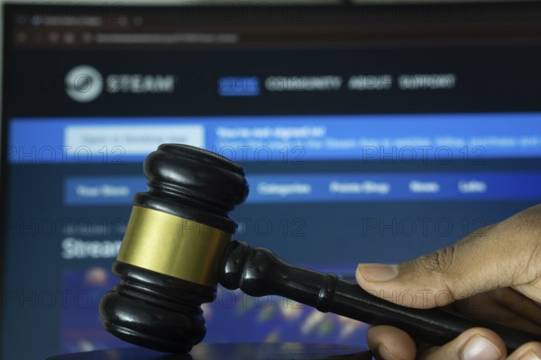 Dhaka, Bangladesh- 20 June 2025: A hand holds a gavel in front of a computer screen displaying steam's website