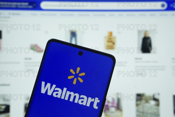 Dhaka, Bangladesh- 15 July 2025: Walmart logo is displayed on a smartphone screen, with the website visible on a computer screen in the background