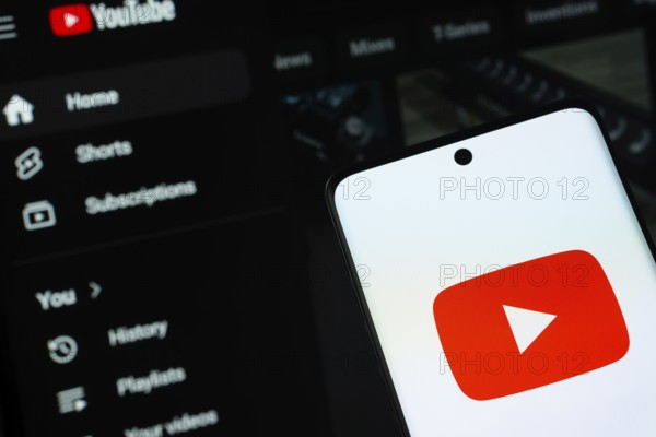 Dhaka, Bangladesh- 10 July 2025: Youtube logo is displayed on a smartphone screen, with the website visible on a computer screen in the background