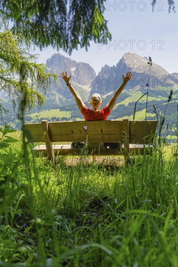 Person on a bench with outstretched arms in front of a mountain landscape, Alpe di Siusi, Dolomites, South Tyrol, Italy