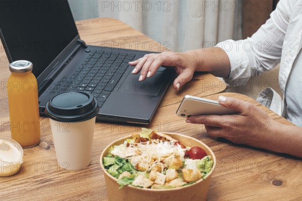 A woman is working on a laptop at home, there is food on the table, salad, coffee and juice, delivery, work at home