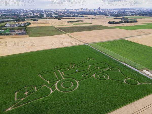 The maize maze of the Maize Spirits near Weißkirchen, near Frankfurt am Main, shows a combine harvester in summer 2025 under the motto Agriculture. The maze opens on 26 July 2025 (aerial photo with a drone), Oberursel Weißkirchen, Hesse, Germany