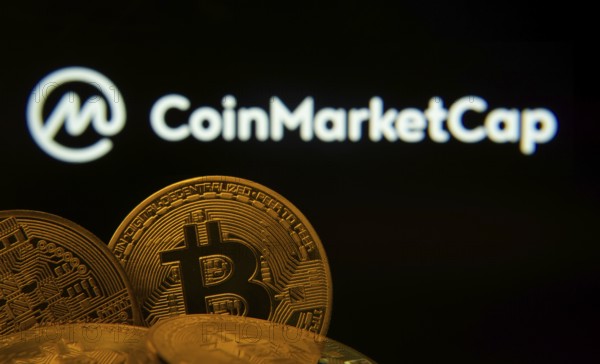 Dhaka, Bangladesh- 27 March 2025: Close-up of Bitcoin coins with the Coinmarketcap logo visible on a screen in the background