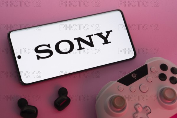 Dhaka, Bangladesh- 02 July 2025: Smartphone with sony logo, game controller, and earbuds on a pink background