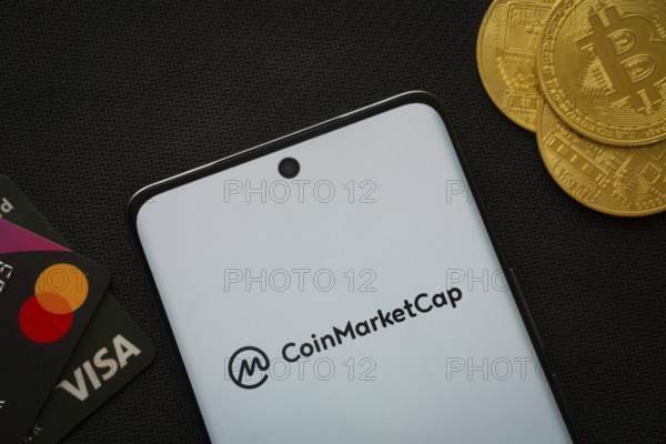 Dhaka, Bangladesh- 22 June 2025: Smartphone displaying Coinmarketcap logo surrounded by Bitcoin coins and payment cards