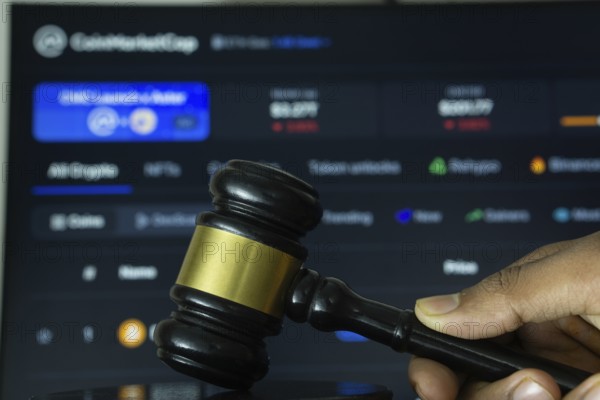 Dhaka, Bangladesh- 20 June 2025: A hand holds a gavel in front of a computer screen displaying Coinmarketcap's website