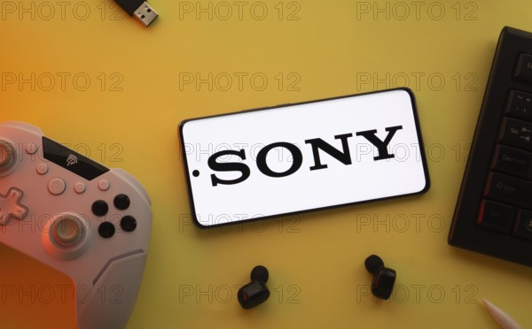 Dhaka, Bangladesh- 03 June 2025: Smartphone with Sony logo, game controller, and earbuds on a yellow background