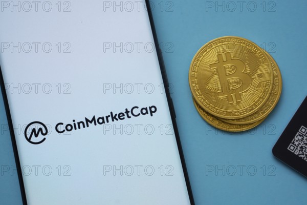 Dhaka, Bangladesh- 22 June 2025: Coinmarketcap logo on smartphone screen near Bitcoin coin and QR code on blue background
