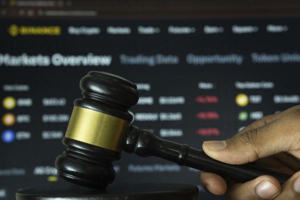 Dhaka, Bangladesh- 20 June 2025: A hand holds a gavel in front of a computer screen displaying binance's website