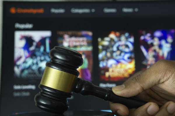 Dhaka, Bangladesh- 20 June 2025: A hand holds a gavel in front of a computer screen displaying Crunchyroll's website