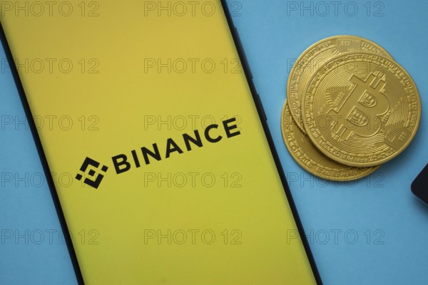 Dhaka, Bangladesh- 22 June 2025: Binance logo on smartphone screen near Bitcoin coin and QR code on blue background