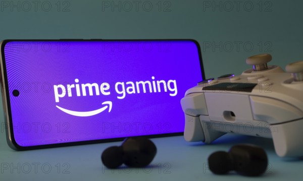 Dhaka, Bangladesh- 22 June 2025: A smartphone with a prime gaming app icon next to a controller and earbuds on a blue surface