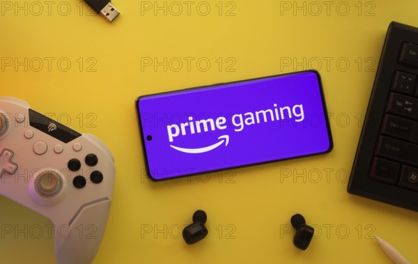 Dhaka, Bangladesh- 22 June 2025: Smartphone with prime gaming logo, game controller, and earbuds on a yellow background