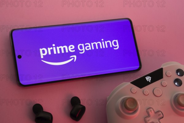 Dhaka, Bangladesh- 22 June 2025: Smartphone with prime gaming logo, game controller, and earbuds on a pink background