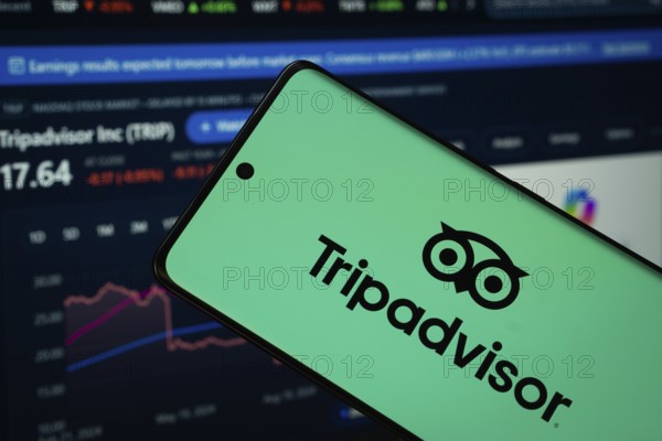Dhaka, Bangladesh- 22 June 2025: Tripadvisor logo is displayed on a smartphone screen, with a stock graph webpage visible on a computer screen in the background