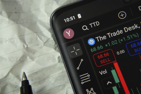 Close-up of a smartphone displaying The Trade Desk stock trading app with a pen and paper nearby