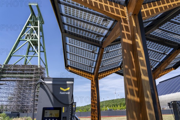 Electric filling station on the site of the former Lohberg colliery in Dinslaken, operated by Fastned, uses electricity from wind power and solar energy, fast-charging columns, with its own solar roof, in the background the 11, 500 square metre solar roof on the colliery's former coal mixing hall, wind farm on the Lohberg slagheap, Lohberg colliery headframe, North Rhine-Westphalia, Germany