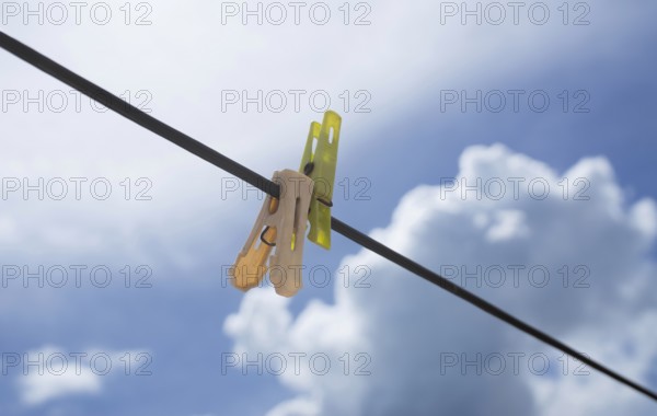 Clothespins on a wire set against a bright blue sky with fluffy clouds