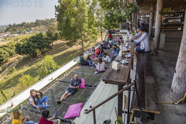 Customers eat, drink and relax on a net suspended over the hillside at the Akha Cottage restaurant and coffee shop in Chiang Rai, Thailand