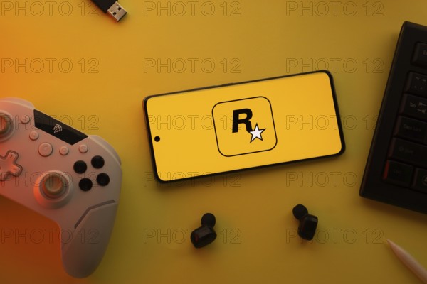 Dhaka, Bangladesh- 17 June 2025: Smartphone with rockstar games logo, game controller, and earbuds on a yellow background