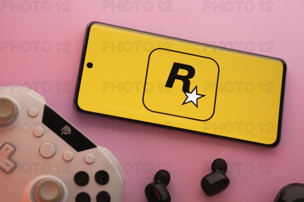 Dhaka, Bangladesh- 17 June 2025: Smartphone with rockstar games logo, game controller, and earbuds on a pink background
