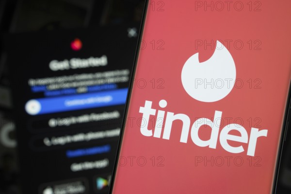 Dhaka, Bangladesh- 18 March 2025: tinder logo is displayed on a smartphone screen, with the tinder login page visible on a computer screen in the background