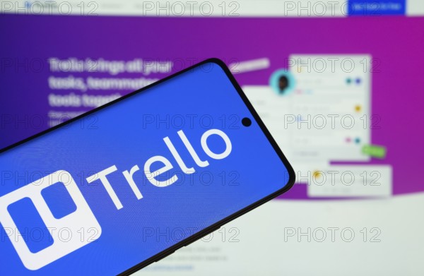 Dhaka, Bangladesh - 18 March 2025: The logo of the trello is displayed on a smartphone screen, and the website trello is visible on a computer screen in the background